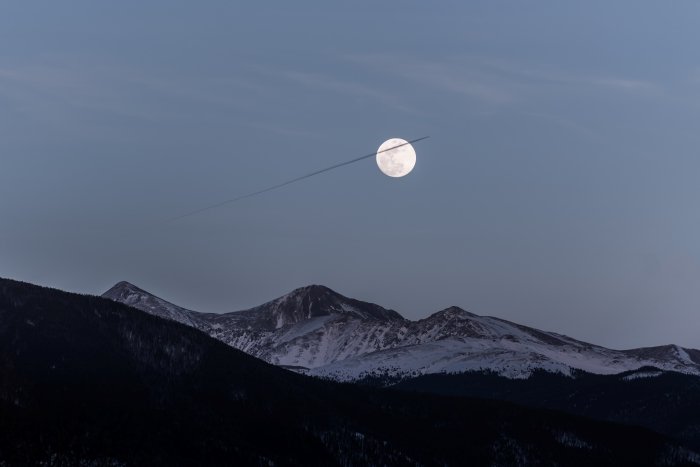 A full moon in a sky above mountains