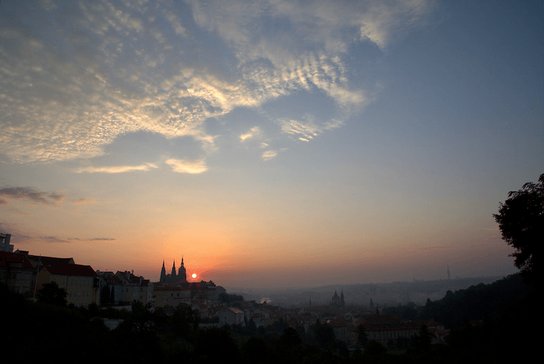 A picture of the sun rising behind Prague castle